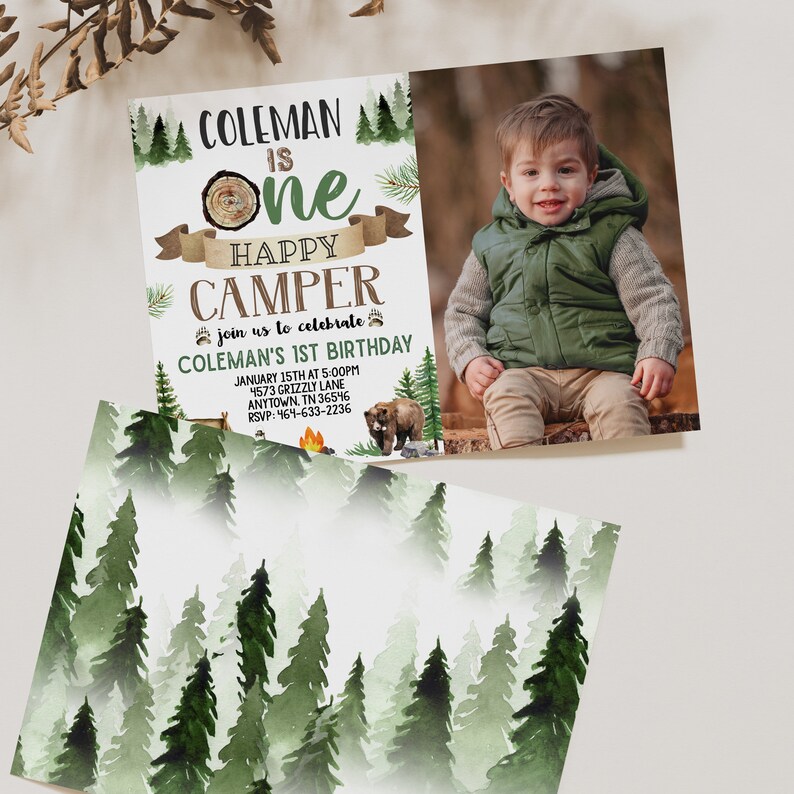 May include: A woodland-themed first birthday invitation for a boy named Coleman. The invitation features a photo of the birthday boy in a green vest, a cartoon bear, and a campfire. The text reads "Coleman is One Happy Camper" and includes details for the party, including the date, time, and location.