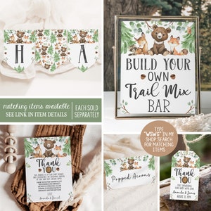 May include: A set of printable baby shower decorations featuring a woodland theme with bears, foxes, and owls. The decorations include a banner, a sign for a trail mix bar, thank you cards, and a sign for popped acorns. The text on the sign reads "Build Your Own Trail Mix Bar".