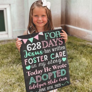 May include: A black chalkboard sign with pink and green decorations announcing that a child has been adopted after 628 days in foster care. The sign reads "FOR 628 DAYS Jesus has written FOSTER CARE in my story Today He Wrote ADOPTED Adelynn Blake Cain JUNE 11TH, 2021".