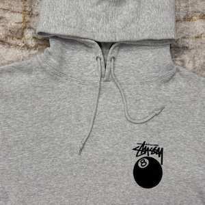 May include: A heather gray hoodie with a drawstring hood. The hoodie features a black and white logo with the number 8 inside a black eight ball.