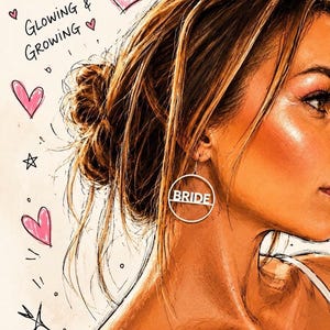 May include: A silver-toned circular earring featuring the word BRIDE in capital letters across the center. The earring is worn by a person with a messy bun hairstyle, set against a background with hand-drawn illustrations of a crown and hearts.