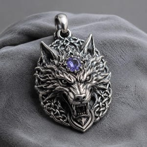 Puede incluir: Un colgante de metal plateado con una cabeza de lobo detallada, dientes al descubierto y textura de pelaje. Una piedra preciosa redonda y facetada de color púrpura está engastada en la frente del lobo, enmarcada por un patrón de nudo celta.