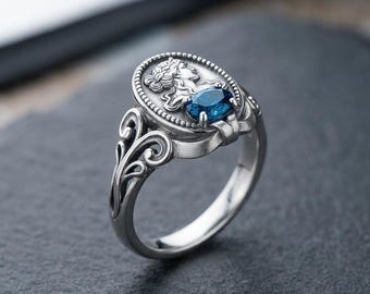 Ein Göttinenring aus Sterlingsilber mit einem blauen Edelstein und durchbrochenen Schriftrollen verleiht ihrem täglichen Stil mythische Eleganz.