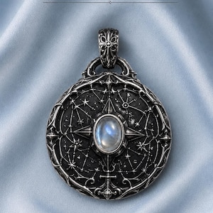 May include: A circular silver pendant featuring the text ArtemisForge at the top. The pendant has a dark, textured surface engraved with a celestial star map and a central oval moonstone cabochon. It includes an ornate, detailed bail.