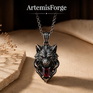 May include: A silver-toned metal pendant necklace featuring a detailed wolf head design with red gemstone eyes and a rectangular red gemstone set at the base. The pendant hangs from a silver chain and includes the text ArtemisForge at the top.