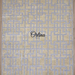 Könnte beinhalten: Rechteckiger Teppich mit einem geometrischen Muster in Hellblau auf beigem Hintergrund. Der Teppich hat einen Fransen am unteren Rand und den Text "Orlina Rugs" in der Mitte.