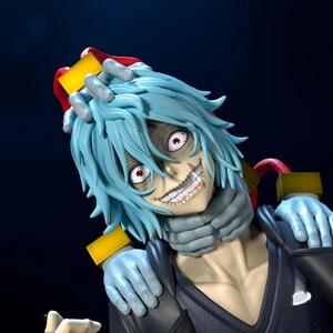 May include: A detailed figurine of a character with pale skin, light blue hair, and red eyes. The character has a wide, unsettling grin with visible teeth. The figure is wearing a dark outfit with a gray scarf and blue gloves. The overall aesthetic is dark and detailed.