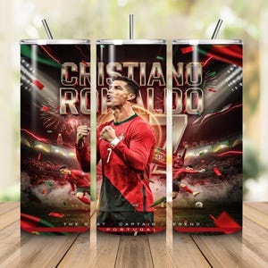 Puede incluir: Un vaso cilíndrico con un gráfico de Cristiano Ronaldo con la camiseta de fútbol roja y verde de Portugal. El diseño incluye el texto CRISTIANO RONALDO, el número 7 y una imagen de un estadio con fuegos artificiales. Incluye tapa y pajita.