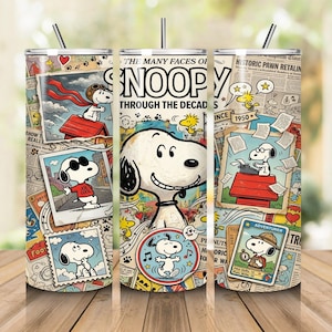 May include: A cylindrical stainless steel tumbler with a straw, featuring a collage of Snoopy and Woodstock illustrations, newspaper clippings, and the text "THE MANY FACES OF SNOOPY THROUGH THE DECADES" printed in black against a multi-colored background.