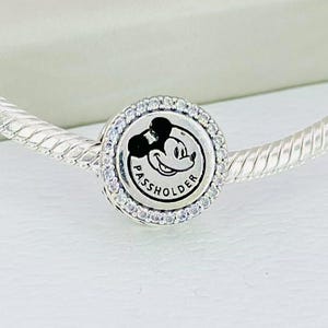 Pu&ograve; includere: Un ciondolo in argento con design circolare, incisione centrale di Mickey Mouse e la scritta PASSHOLDER. Il ciondolo &egrave; bordato da un anello di piccole pietre chiare e scintillanti ed &egrave; infilato su un bracciale a catena a serpente.