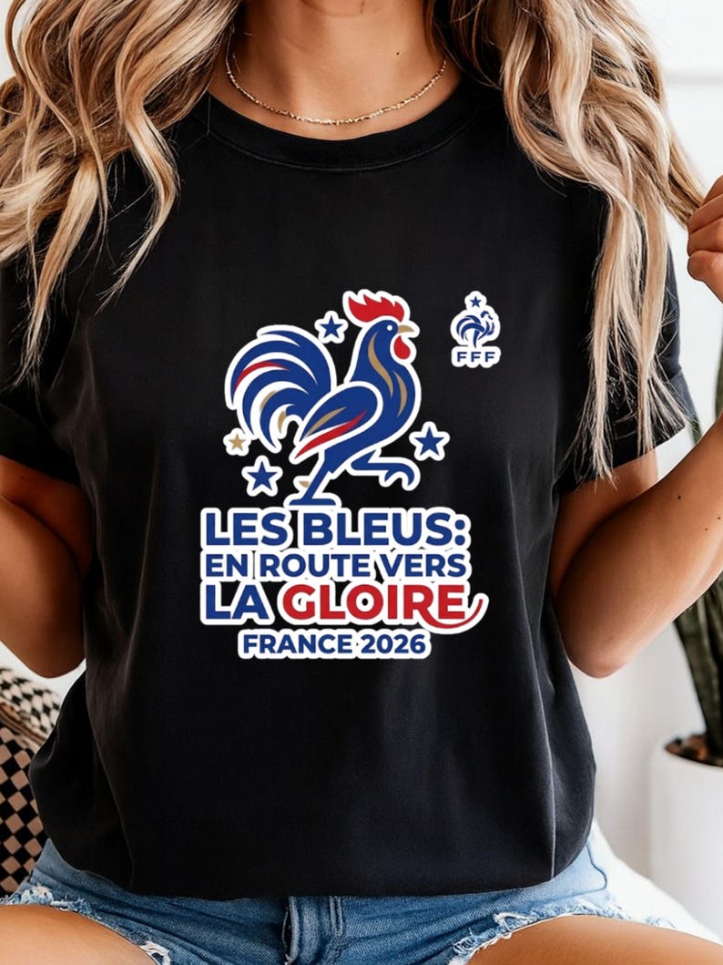 Pu&ograve; includere: T-shirt nero con un disegno di gallo blu, bianco e rosso e la scritta "LES BLEUS: EN ROUTE VERS LA GLOIRE FRANCE 2026". Include il logo FFF e stelle. Un capo a tema calcio francese.