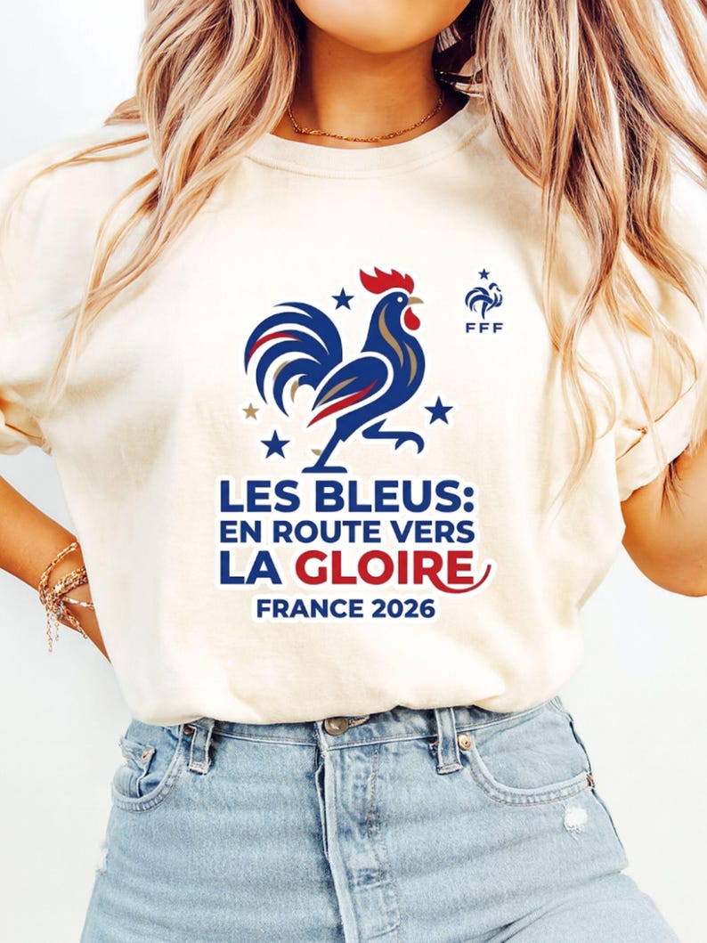 Pu&ograve; includere: T-shirt color crema con grafica di gallo blu, bianco e rosso, stelle e la scritta "LES BLEUS: EN ROUTE VERS LA GLOIRE FRANCE 2026". La maglietta include anche il logo FFF.