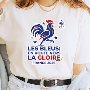 Pu&ograve; includere: T-shirt bianco con grafica di gallo blu, rosso e oro e la scritta "LES BLEUS: EN ROUTE VERS LA GLOIRE FRANCE 2026". La maglietta ha anche il logo FFF ed &egrave; uno stile girocollo.