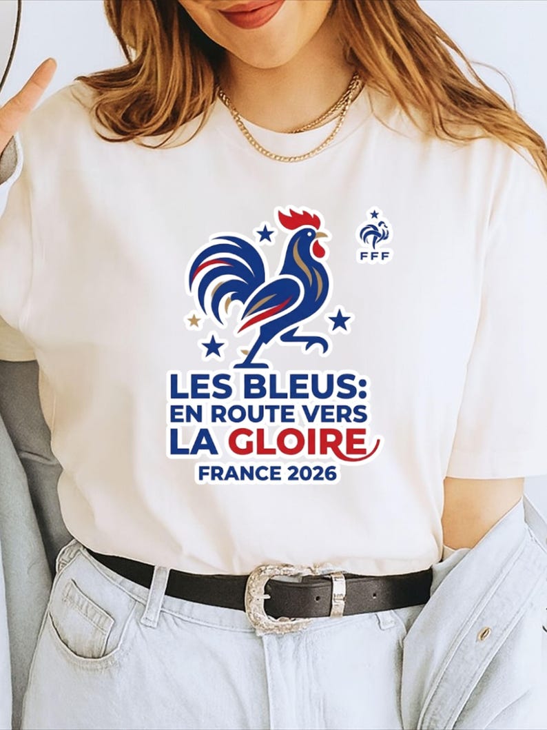 Pu&ograve; includere: T-shirt bianco con grafica di gallo blu, rosso e oro e la scritta "LES BLEUS: EN ROUTE VERS LA GLOIRE FRANCE 2026". La maglietta ha anche il logo FFF ed &egrave; uno stile girocollo.