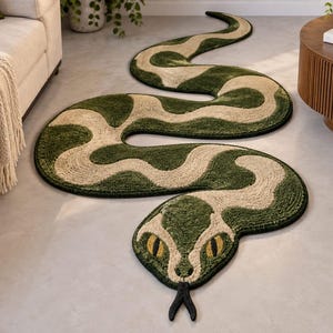 Puede incluir: Una alfombra larga y sinuosa con forma de serpiente que presenta un pelo texturizado en verde bosque profundo y beige claro. La alfombra tiene una cabeza distintiva con ojos amarillos, pupilas negras y una lengua negra bífida.