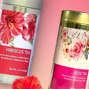 Può includere: Due barattoli di tè cilindrici in metallo del marchio Namhya. Il barattolo a sinistra presenta un'illustrazione di ibisco rosso e il testo Hibiscus Tea, Net Wt. 1.41 oz (40g). Il barattolo a destra mostra rose e il testo Rose Tea.