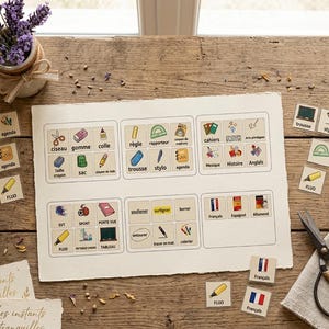 May include: A set of educational flashcards featuring French school vocabulary and illustrations. The cards display items like scissors, glue, and notebooks, alongside action verbs and subject names. The set includes a large sheet with grid-organised cards and several individual loose cards, all printed on off-white paper with a deckled edge.