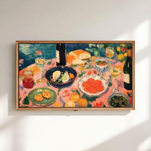 Peut inclure: Impression d'art encadrée d'une nature morte. Une table est dressée avec de la nourriture et des boissons, dont des bouteilles de vin, des verres, du pain et divers plats. La nappe est rose avec des motifs floraux. L'œuvre est dans un cadre en bois.