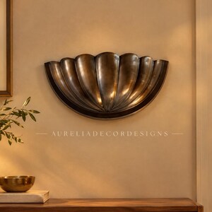 Könnte beinhalten: Eine halbkreisförmige Wandleuchte mit einer metallischen Bronzefläche und einem geriffelten, muschelartigen Design mit vertikalen Rippen. Der Text AURELIADE CORDESIGNS ist unter der Leuchte zentriert. Die Oberfläche ist glatt und geschwungen.
