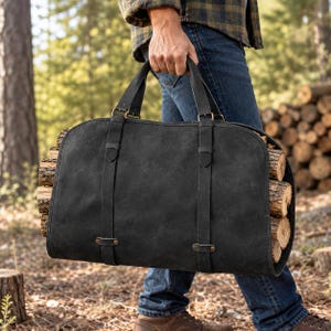 May include: A black canvas firewood carrier with two sturdy handles and two vertical straps featuring metal buckles. The carrier is filled with stacked wooden logs, showcasing a durable design intended for transporting firewood with ease.