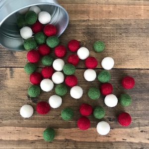 May include: A metal bucket spilling out red, white, and green felt balls. The balls are scattered on a wooden surface.