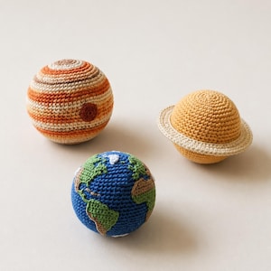 May include: Three crocheted planet toys: Jupiter with orange and tan stripes, Earth with blue oceans and green continents, and Saturn with a yellow body and a tan ring. These soft toys are perfect for educational play.