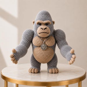 May include: A handcrafted crochet gorilla toy in grey and tan. The gorilla has a silver pendant necklace and is posed with its arms outstretched. The toy is sitting on a gold-legged table.