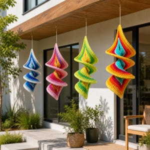 Könnte beinhalten: Vier farbenfrohe, spiralförmige Häkelornamente, die an einem Holzbalken hängen. Die Ornamente weisen eine Vielzahl von Farben auf, darunter Blau, Rosa, Grün und Gelb, mit einem weißen Rand. Sie sind an dünnen, goldfarbenen Drähten aufgehängt und schaffen eine skurrile Außendekoration.