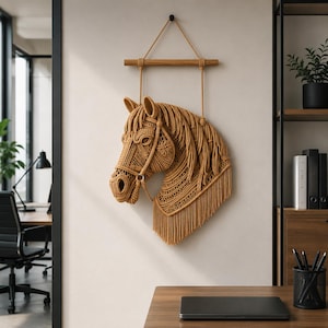 Peut inclure: Décoration murale en forme de tête de cheval tissée, dans des tons de beige et de marron. La tête de cheval est ornée d'une bride et d'une crinière flottante, suspendue à une cheville en bois et à une corde. L'œuvre est exposée sur un mur neutre.