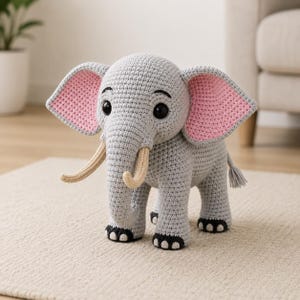 May include: A gray crocheted elephant toy with large black eyes, pink-lined ears, and ivory tusks. The elephant has a gray tail and black accents on its feet. This handmade stuffed animal is a charming decorative piece.