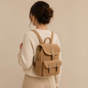 Könnte beinhalten: Ein beigefarbener Rucksack aus gewebtem Material mit Klappenverschluss und zwei Vordertaschen. Der Rucksack hat verstellbare Träger und einen oberen Griff. Die Tasche besteht aus gewebtem Material und hat lederartige Akzente. Die Person trägt einen cremefarbenen Pullover.