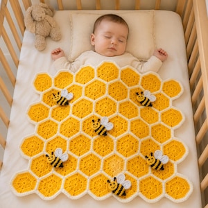 Puede incluir: Un bebé durmiendo en una cuna de madera, cubierto con una manta de ganchillo amarilla y blanca. La manta está diseñada con un patrón de panal y adornada con varias aplicaciones de abejas. Un conejito de peluche está en la cuna.