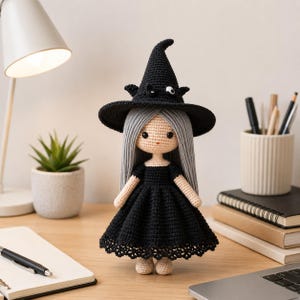 Könnte beinhalten: Handgefertigte Häkelpuppe als Hexe, mit schwarzem Kleid und Hut. Die Puppe hat lange graue Haare und steht auf einer Holzoberfläche. Eine charmante Halloween-Dekoration. Die Puppe ist etwa 20 cm groß.