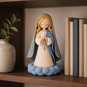 Puede incluir: Muñeca de ganchillo hecha a mano de la Virgen María, con un vestido color crema, una capa azul con ribetes dorados y un collar con una cruz dorada. La muñeca tiene cabello rubio y está sobre una base azul en forma de nube.