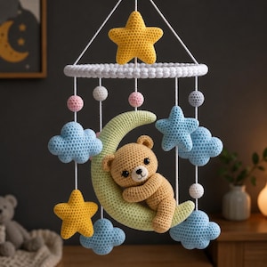 Puede incluir: Móvil de bebé hecho a mano con ganchillo, con un osito de peluche sobre una luna creciente. Incluye estrellas amarillas, nubes azules y esferas pastel. El móvil está suspendido de un anillo blanco. Medidas en cm.
