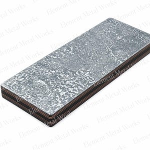 May include: A rectangular metal billet featuring a complex, swirling gray and silver Damascus pattern on the top surface, with visible layered construction along the sides showing alternating dark and copper-colored metallic bands.