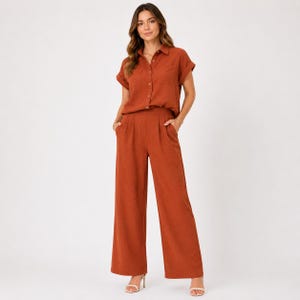 May include: A rust-colored two-piece set consisting of a short-sleeved button-down shirt with a collar and a chest pocket, paired with matching high-waisted wide-leg trousers featuring side pockets and a pleated front design.