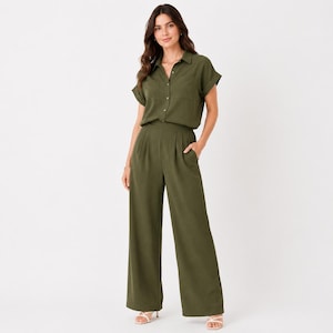 May include: An olive green jumpsuit featuring a short-sleeved button-down bodice with a collar and two chest pockets. The garment includes a high-waisted design with pleated details at the front and wide-leg trousers that fall to the floor.