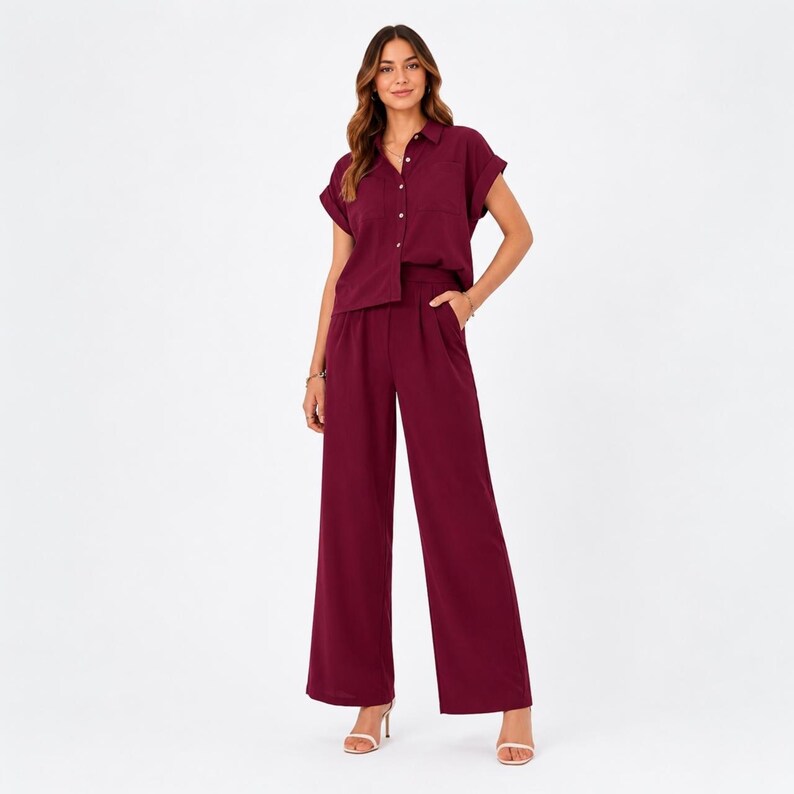 May include: A deep burgundy two-piece set consisting of a short-sleeved button-down shirt with a collar and a chest pocket, paired with matching high-waisted wide-leg trousers featuring side pockets and a clean, straight-cut hemline.
