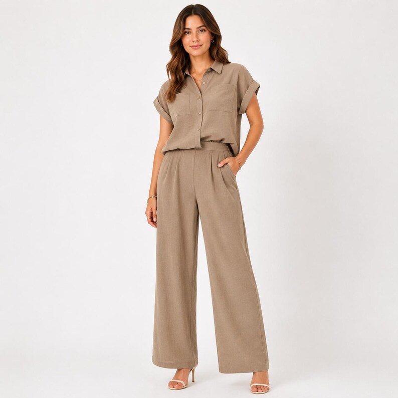 May include: A taupe two-piece set consisting of a short-sleeved button-down shirt with a collar and a chest pocket, paired with matching high-waisted wide-leg trousers featuring side pockets and a pleated front design in a solid neutral color.