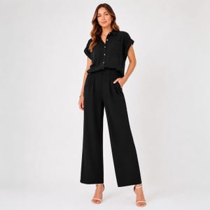 May include: A black two-piece set consisting of a short-sleeved button-down shirt with a collar and a front pocket, paired with high-waisted wide-leg trousers featuring side pockets and a clean, solid-colored finish throughout the garment.