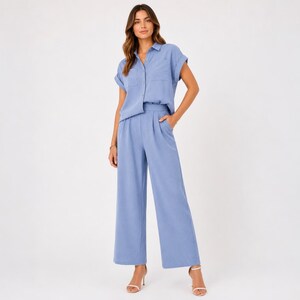 May include: A light blue two-piece set consisting of a short-sleeved button-down shirt with a collar and a chest pocket, paired with matching high-waisted wide-leg trousers featuring front pleats and side pockets in a solid light blue color.
