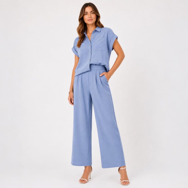 May include: A light blue two-piece set consisting of a short-sleeved button-down shirt with a collar and a chest pocket, paired with matching high-waisted wide-leg trousers featuring front pleats and side pockets in a solid light blue color.