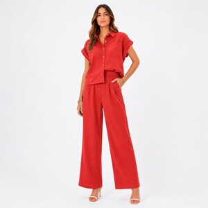 May include: A two-piece set consisting of a short-sleeved, button-down shirt with a collar and two chest pockets, paired with matching high-waisted, wide-leg trousers featuring side pockets, all rendered in a solid, vibrant brick-red color.