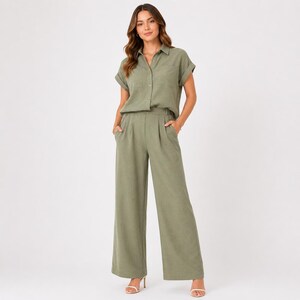 May include: An olive green two-piece set consisting of a short-sleeved button-down shirt with a collar and two chest pockets, paired with matching high-waisted wide-leg trousers featuring pleats at the waist and side pockets.
