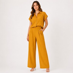 May include: A mustard yellow two-piece set consisting of a short-sleeved button-down shirt with a collar and a chest pocket, paired with high-waisted wide-leg trousers featuring front pleats and a clean, solid-colored finish throughout the garment.