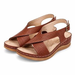 Op de afbeelding: Een paar bruine sandalen met een geperforeerd kruisbandontwerp aan de bovenkant. De sandalen hebben een open teen, een hielbandje met een kleine bronskleurige metalen gesp en een lichtgekleurd voetbed met demping.