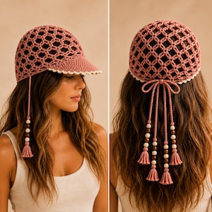 Può includere: Un berretto all'uncinetto color rosa polvere con un motivo a rete traforato, una visiera piena con bordo bianco smerlato e lunghi cordini pendenti decorati con perline di legno e nappe abbinate che scendono dai lati e dal retro.