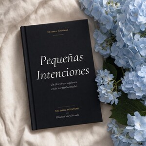 Puede incluir: Un libro de tapa dura negro titulado Pequeñas Intenciones con texto blanco en fuente serif y detalles dorados. La portada incluye el texto The Small Intentions, Un diario para quienes están cargando mucho y Elizabeth Mary Brizuela junto a flores.