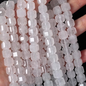 Puede incluir: Múltiples hilos de cuentas de cuarzo blanco translúcido facetado dispuestas en filas verticales. Cada cuenta presenta una forma hexagonal distintiva con superficies pulidas que reflejan la luz, creando una apariencia brillante y clara en todo el conjunto.